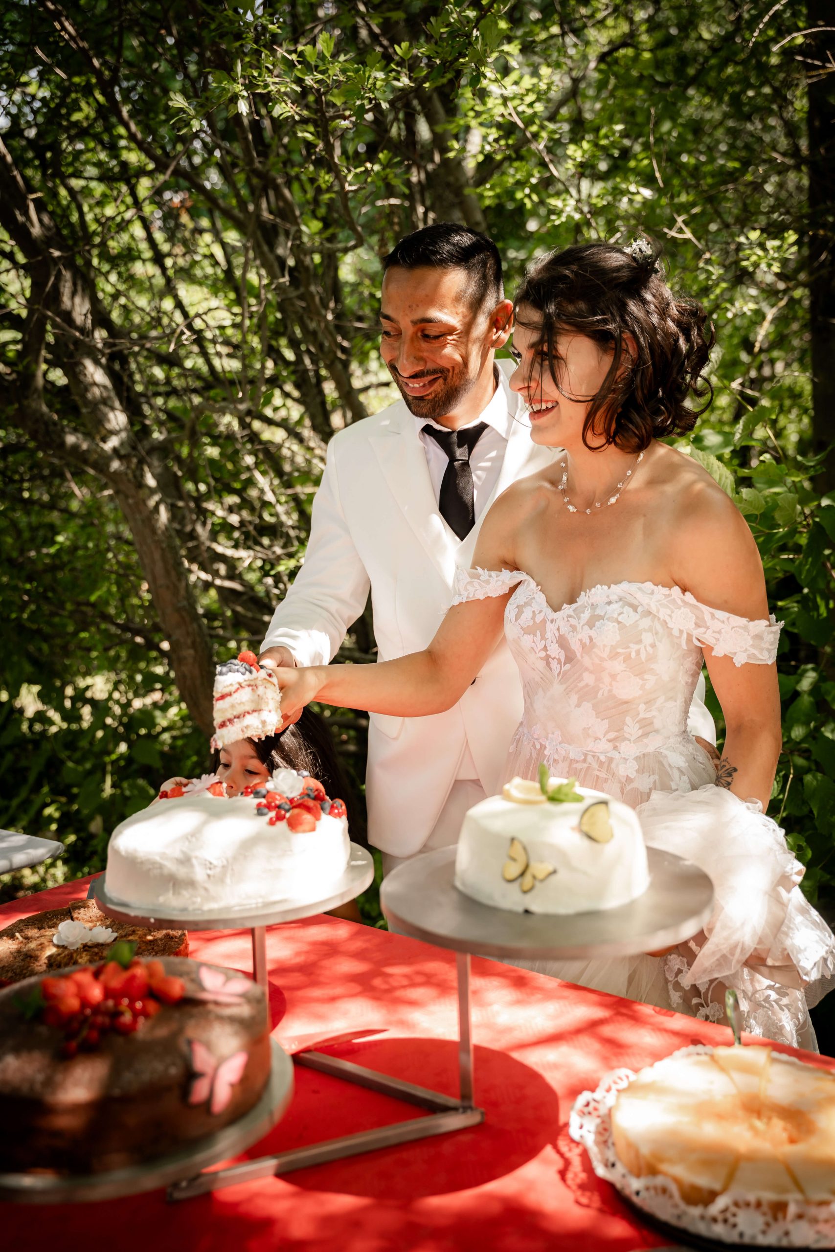 Das Brautpaar lächelt beim Tortenanschnitt im Garten. Fotografiert von Anke Hartl. Hochzeitsfotografin Freiberg und Dresden.