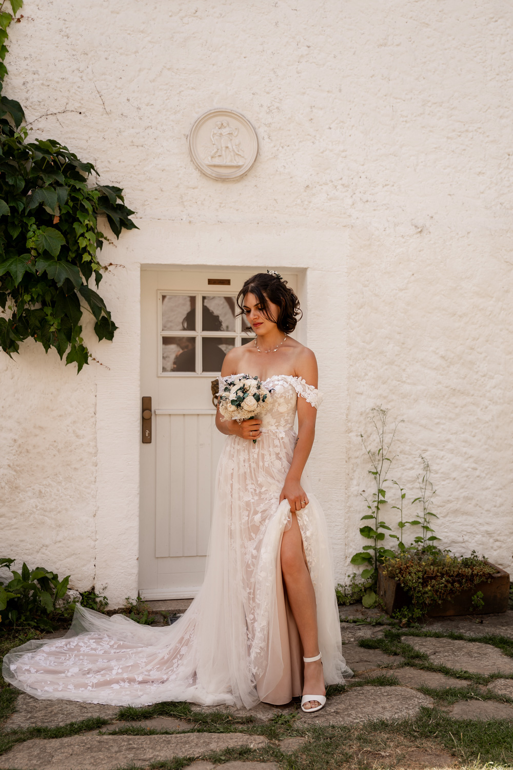 Die Braut steht vor dem Landhaus mit dem Brautstrauß in der Hand und präsentiert ihr wunderschönes Kleid. Fotografiert von Anke Hartl von Echte Hochzeitsmomente