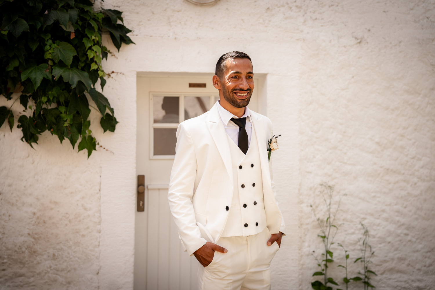 Der Bräutigam der lächelnd seinen schicken weißen Anzug präsentiert. Fotografiert von Anke Hartl von Echte Hochzeitsmomente.